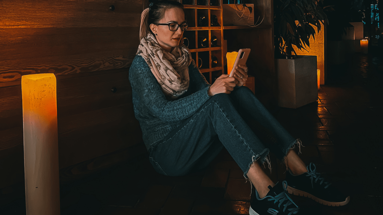 Tetyana is sitting on the floor. She is reading something on her mobile phone. The lights are off. But there is one huge lit candle on the left. This picture is used for the blog post for the Bloganuary challenge from WordPress.